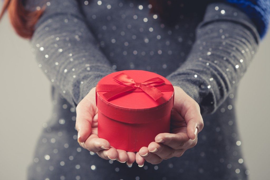 Beautiful small round red festive Christmas gift box cradled in the cupped hands of a woman wearing a spangly top twinkling in the light, close up cropped torso view