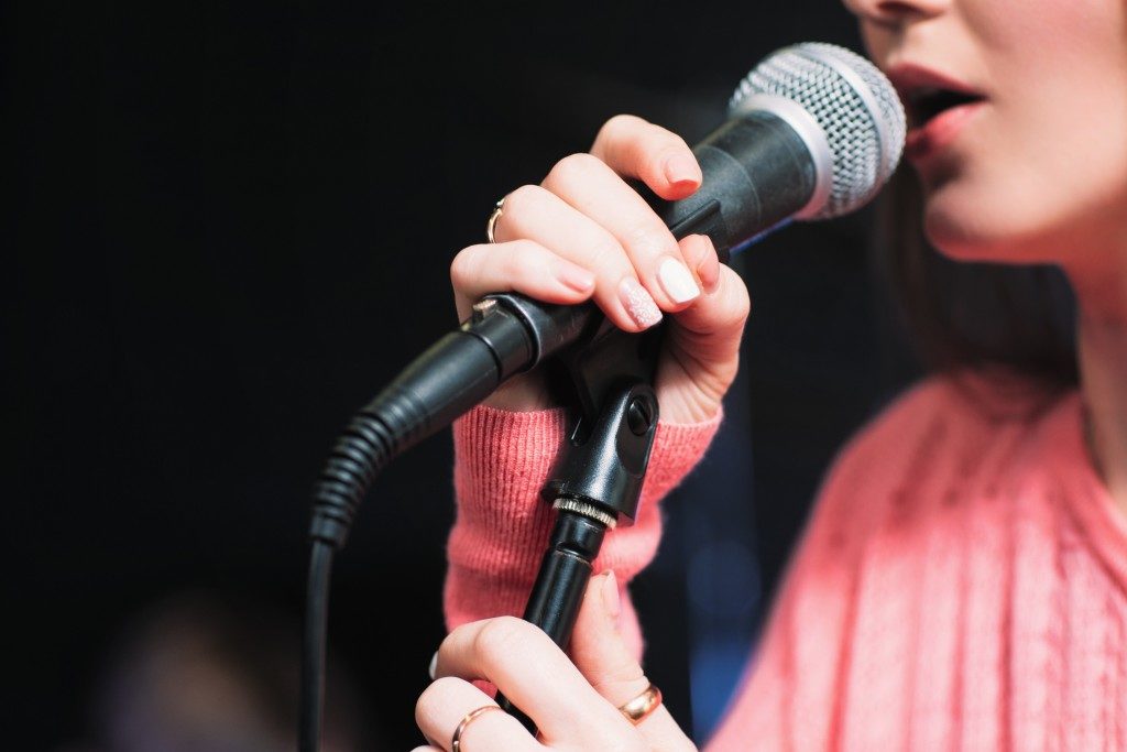 Cropped image of female singer in pink dress , singing into a microphone, holding mic with two hands.