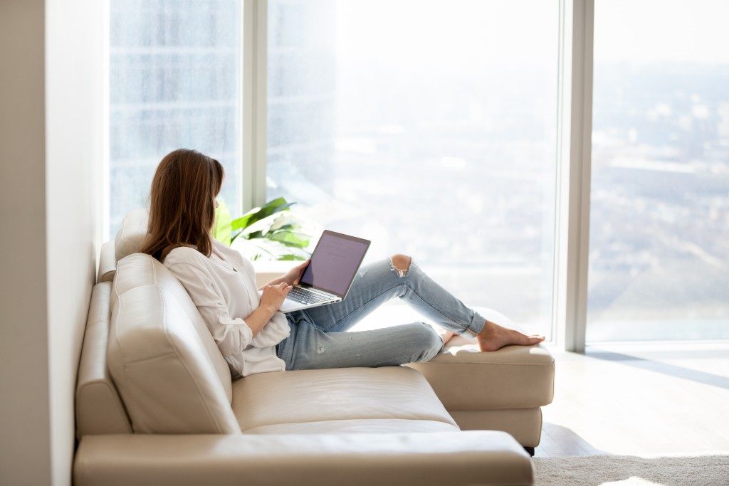 woman uhsing her laptop while lounging on couch